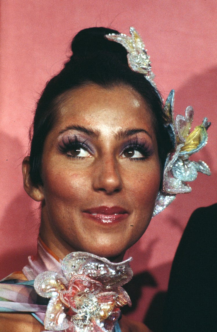 Cher with a top bun accessorized with embellished flowers and a flower around her neck at the Ocars 