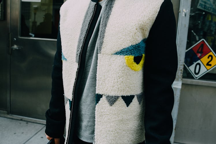 A close-up of a person in a white-black fleece jacket with eye and teeth shaped elements