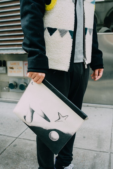 A man standing in a black-white fleece jacket while holding a black-white purse 