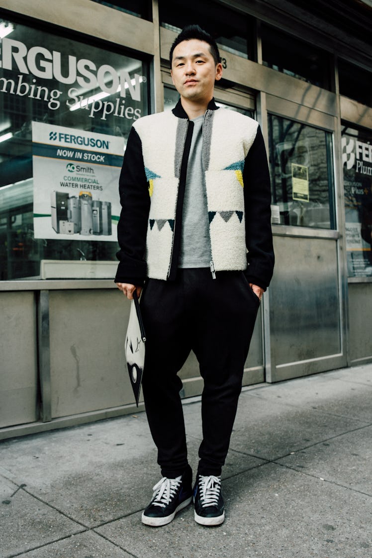 A man in a white-black fleece jacket with eye and teeth shaped elements and black trousers