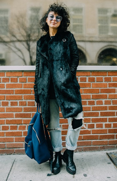 A woman in a black fur coat, blue denim jeans, black boots and a blue backpack at Hood by Air