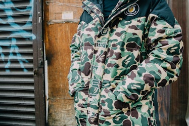 A close-up of a man wearing a camo print puffer jacket with his hands in his pockets