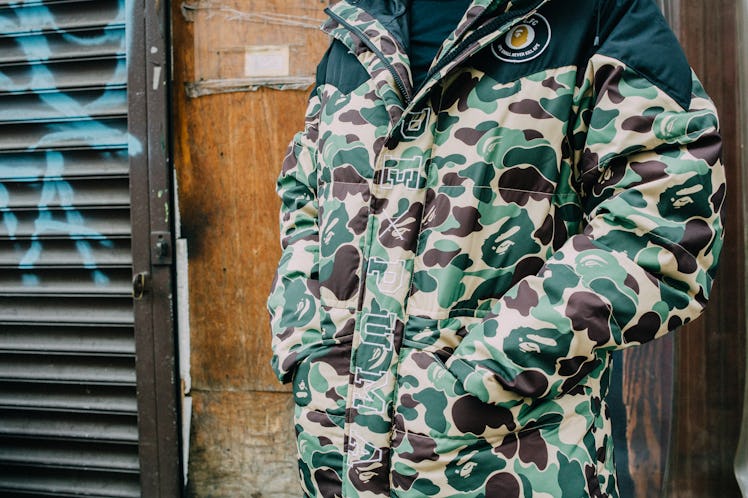 A close-up of a man wearing a camo print puffer jacket with his hands in his pockets