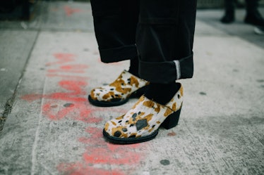 A close-up of a person wearing brown-white-black cow print mid heel shoes at Hood by Air