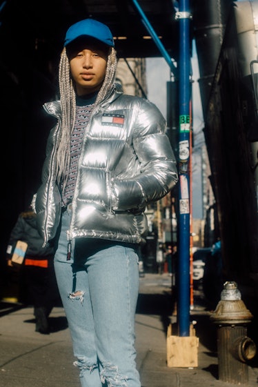 A woman in a silver metallic puffer jacket, blue denim jeans, a navy-white top and a blue cap at Air...