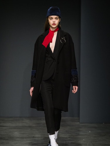 A model wearing a black suit and coat and a red scarf on the runway