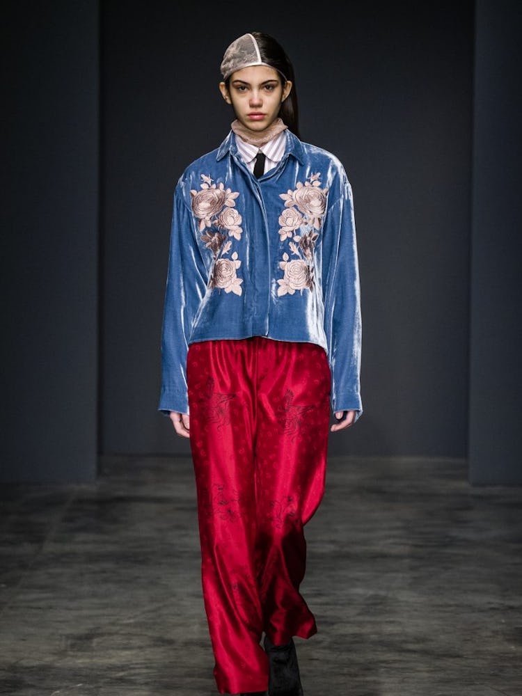A model wearing a velvet blue floral jacket and red satin trousers on the runway