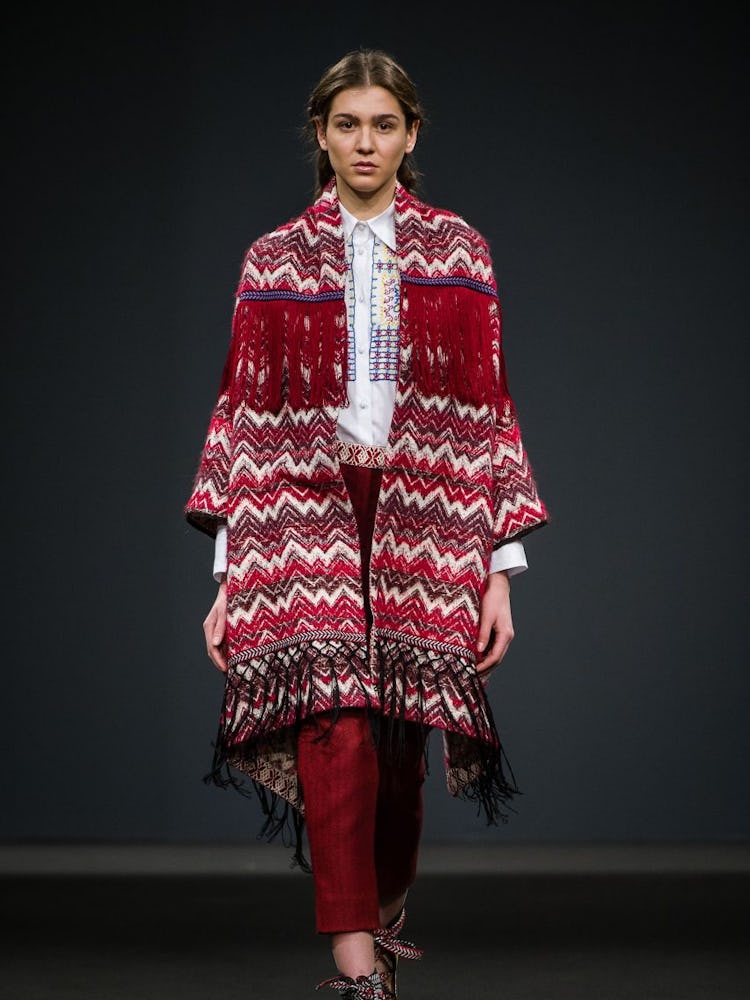 A model wearing a red-white patterned fringed coat and red trousers on the runway