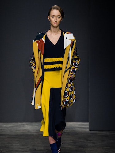 A model wearing a black-yellow dress and geometric print jacket on the runway