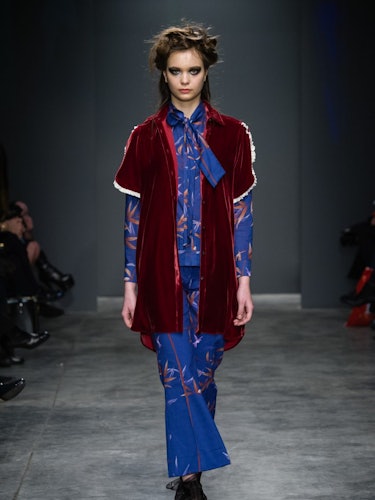 A model in a floral blue sating shirt and pants and a burgundy velvet vest on the runway