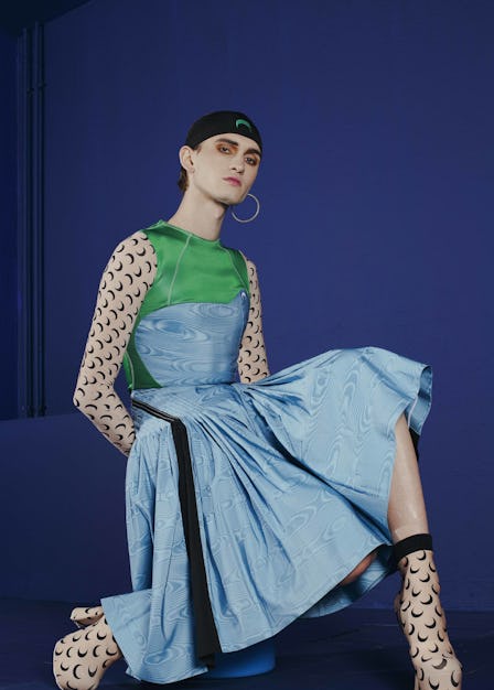 A model sitting in a blue-green dress with a half-moon print on sleeves and boots by Marine Serre at...