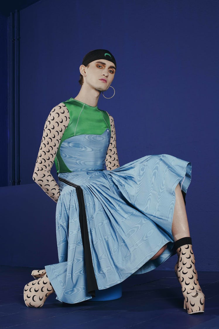 A model sitting in a blue-green dress with half-moon print sleeves and boots by Marine Serre at the ...