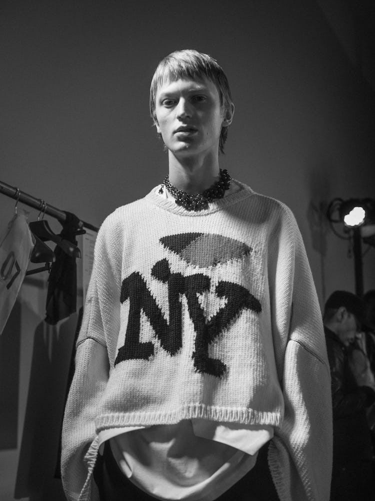 A model wearing a white sweater with 'NY' embroidered, backstage at Raf Simons' Fall 2017 show