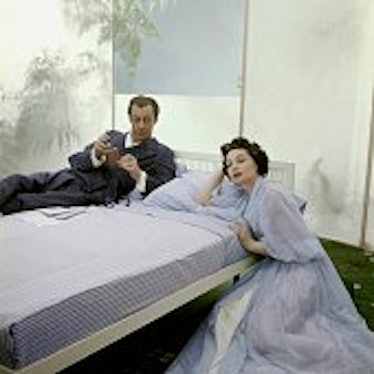 Mr. and Mrs. Rex Harrison posing on and beside a bed.