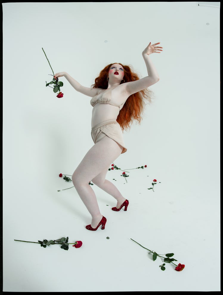 A red-haired model posing in cream satin underwear with red roses around her