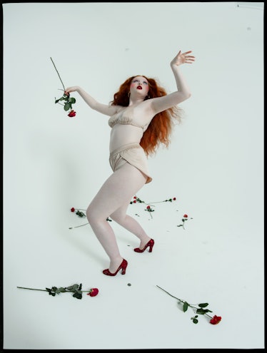 A red-haired model posing in cream satin underwear with red roses around her