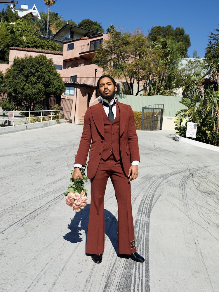 A man in a brown suit holding a bouquet of pink roses on the street