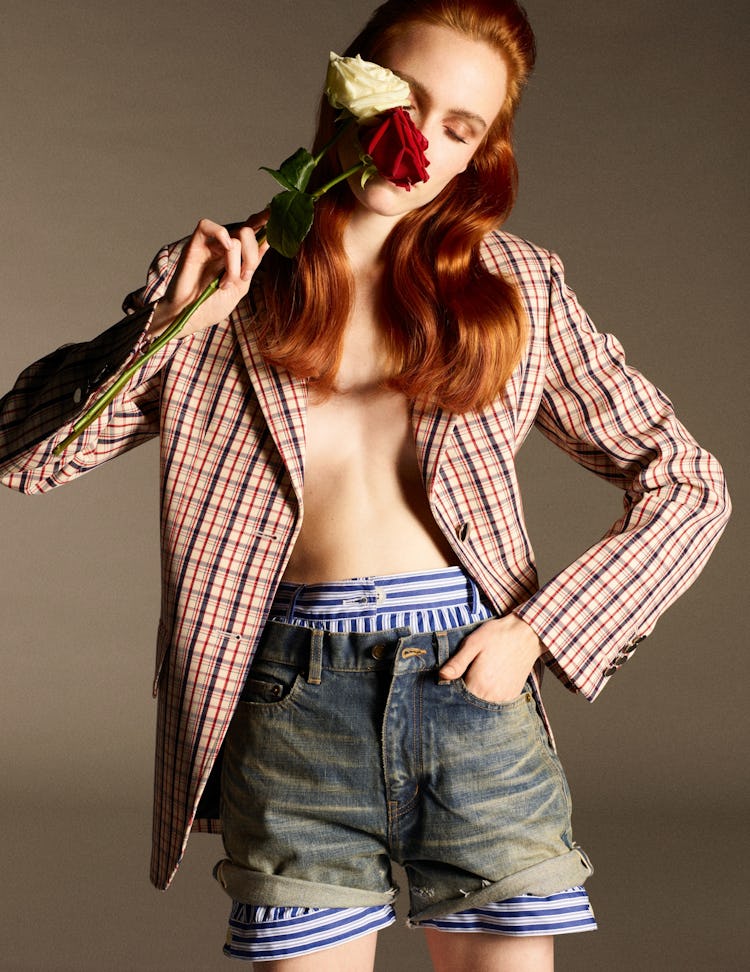 A red-haired model in a checked blazer and shorts holding roses next to her face