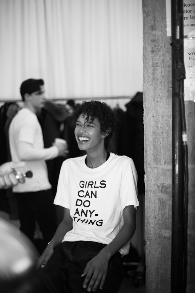 Dilone sitting in a "girls can do anything" shirt, smiling backstage at the Zadig & Voltaire show 