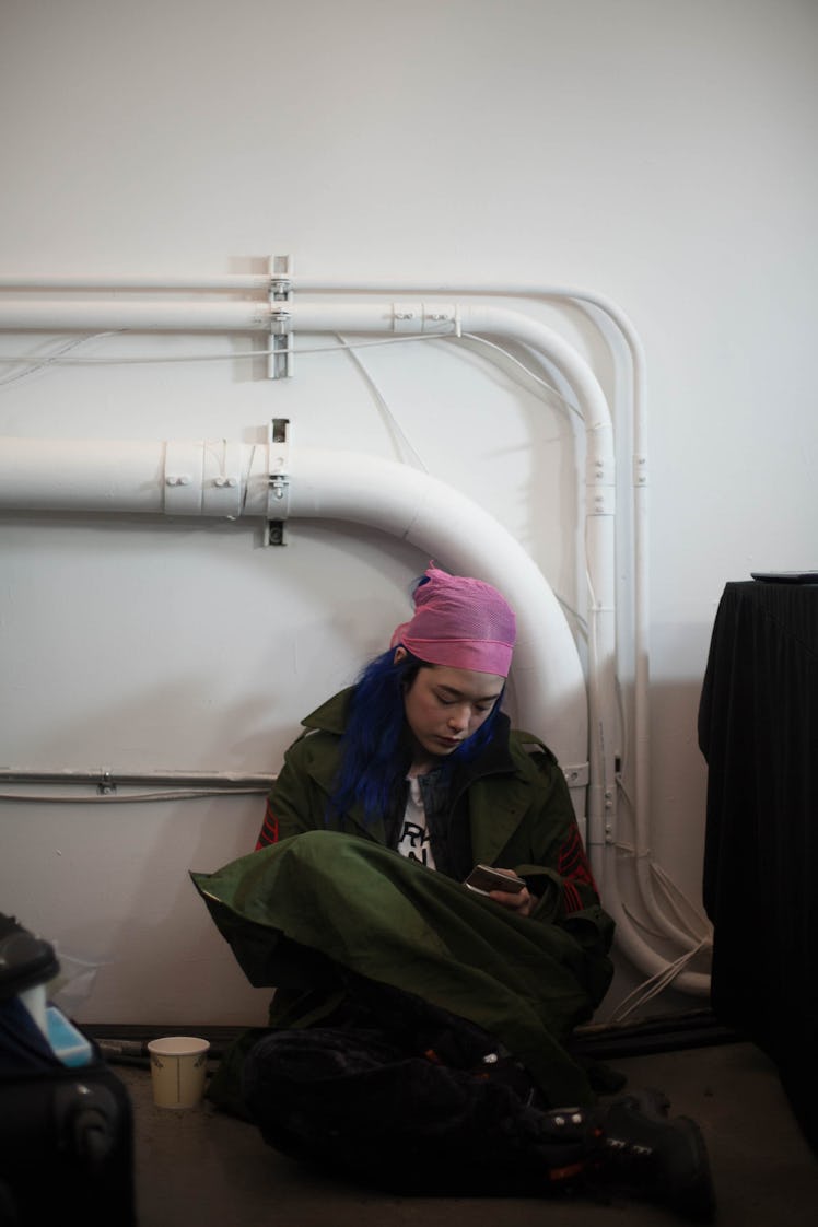 A model sitting on the floor wearing a pink doo-rag using her phone backstage at the Zadig & Voltair...