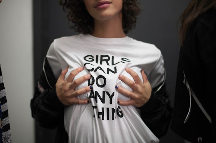 A model wearing a "girls can do anything" shirt and holding her breasts 