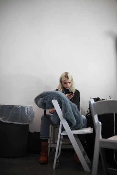 A model sitting, using her phone backstage at the Zadig & Voltaire Fall 2017 show 