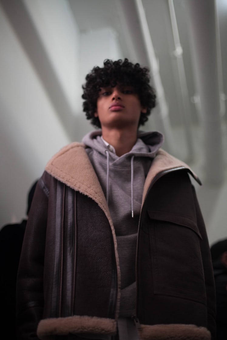 A model backstage at the Zadig & Voltaire show in a grey sweatshirt and a black jacket with brown fu...