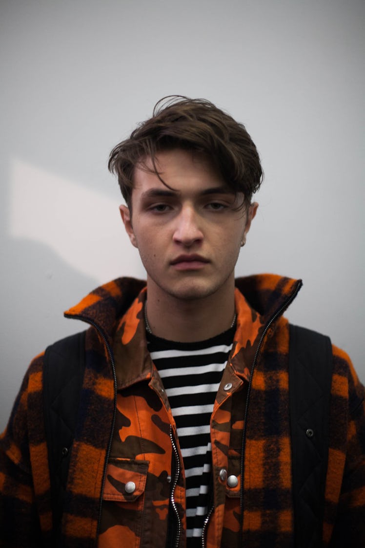 A model backstage at the show posing in a plaid orange jacket and striped black and white shirt 