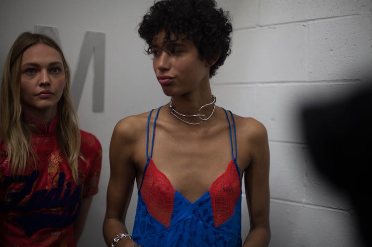 A model in a blue top with red lace walking with a model in a maroon top backstage at the show 