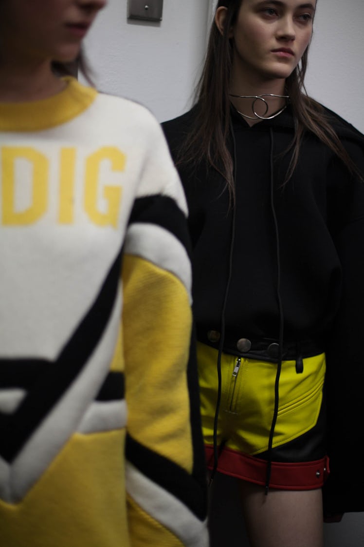 A model in a black sweater and yellow shorts with red and black, walking behind a model in a yellow ...