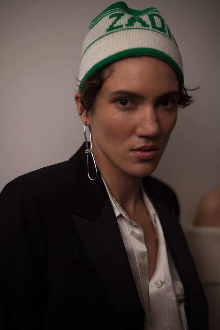 A model in a green and white beanie, and a black blazer with a white button-up underneath 