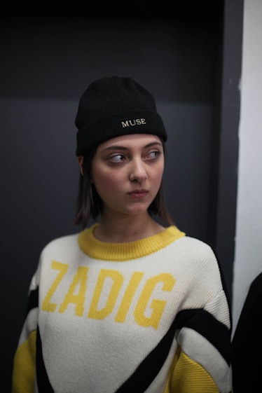 A model in a white and yellow sweater with black stripes that says "Zadig" on it and a black beanie ...