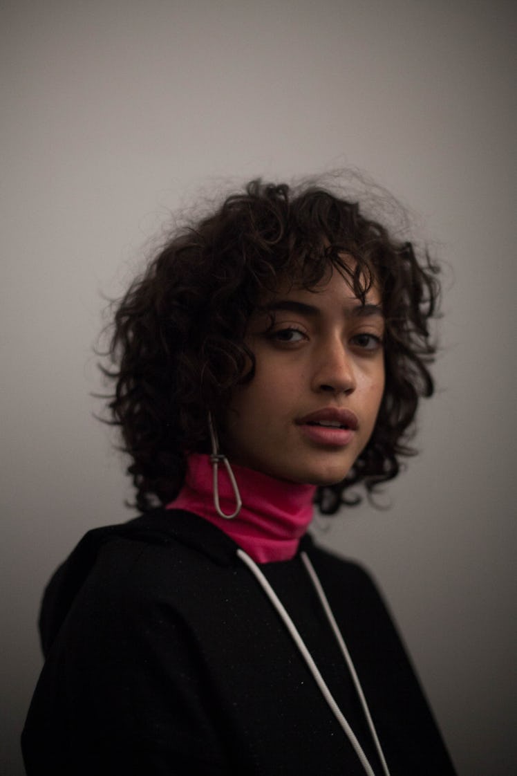 A model in a black hoodie with a pink turtleneck underneath, looking directly at the camera 