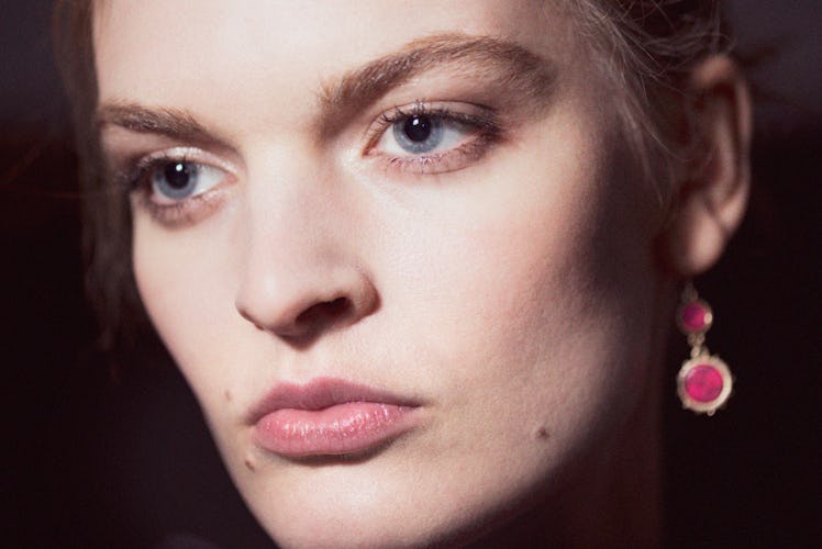 A close-up portrait of a model with pink earrings backstage at Monse Fall 2017