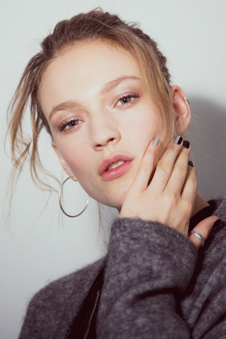 A close-up portrait of a model with golden hoop earrings in a grey sweater backstage at Monse Fall 2...