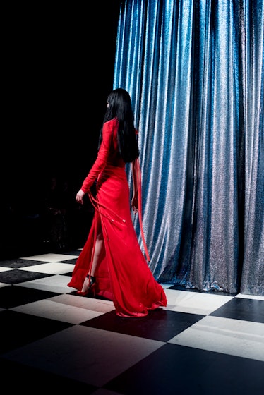 A model with long black hair walking in a red dress backstage at Monse Fall 2017
