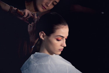 A model sporting orange eyeshadow getting her hair done by a hairstylist backstage at Oscar de la Re...
