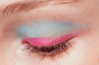 A close-up of a model's semi closed eye wearing blue and pink eyeshadow backstage at Oscar de la Ren...