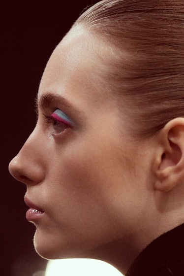 A side close-up profile portrait of a model wearing blue-pink eyeshadow backstage at Oscar de la Ren...