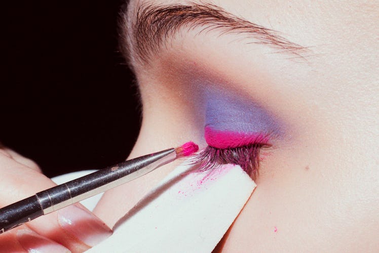 A close-up of a make-up artist applying blue-pink eyeshadow on a model backstage at Oscar de la Rent...