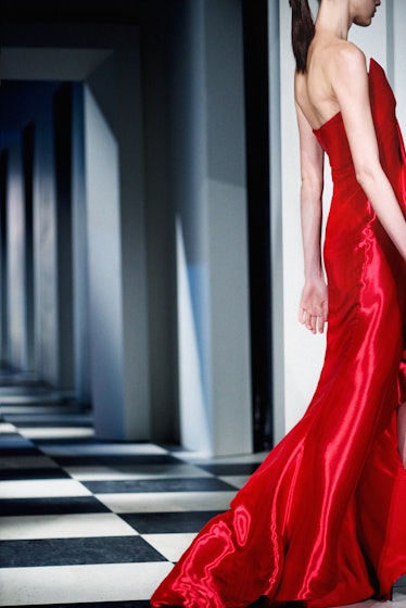 A model walking in a long satin red gown backstage at Oscar de la Renta Fall 2017