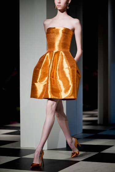 A model walking in an orange satin dress backstage at Oscar de la Renta Fall 2017