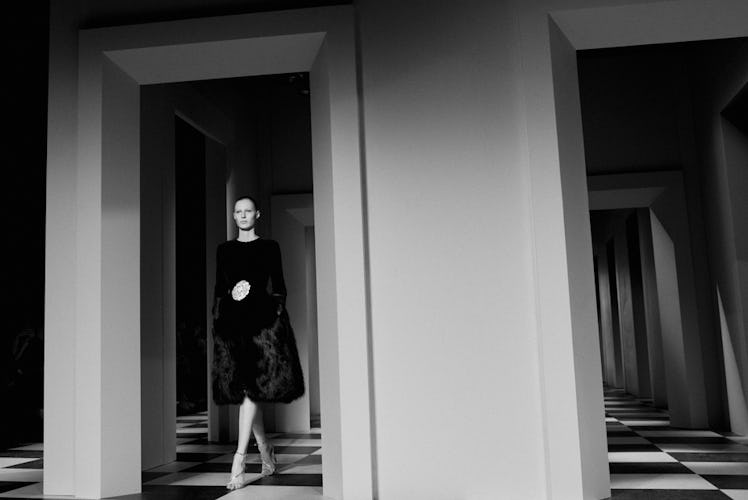 A model walking in a black dress and jacket backstage at Oscar de la Renta Fall 2017