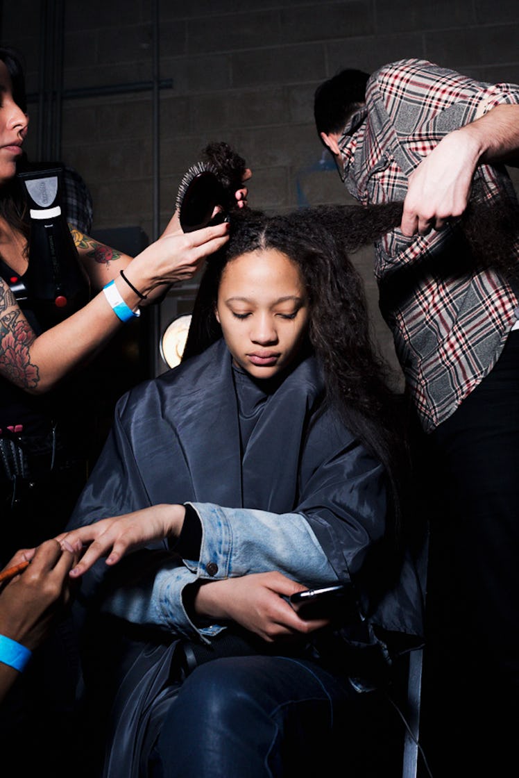 A model in a navy jacket getting her hair done by hairstylists backstage at Oscar de la Renta Fall 2...