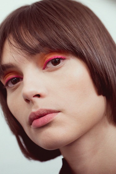 A close-up portrait of a brunette model with orange-pink eyeshadow backstage at Oscar de la Renta Fa...