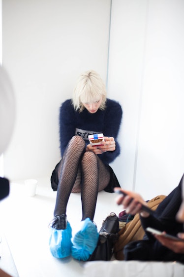 A blonde female model sitting while wearing a black fur shirt and black skirt
