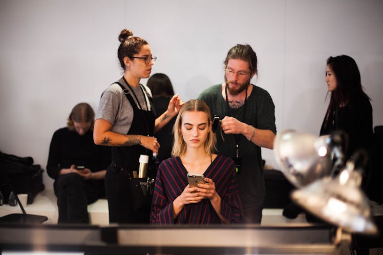 A blonde female model using her mobile phone while hairdressers are making her hairstyle