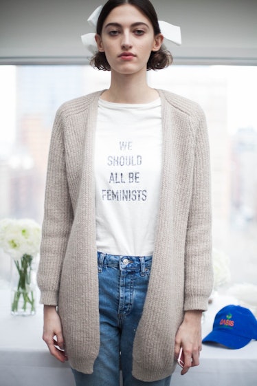 A black-haired woman wearing a white shirt with "WE SHOULD ALL BE FEMINISTS" text 