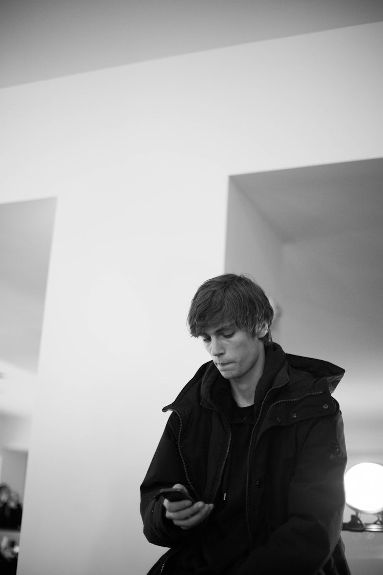 A young man sitting while wearing a black jacket and typing on his phone