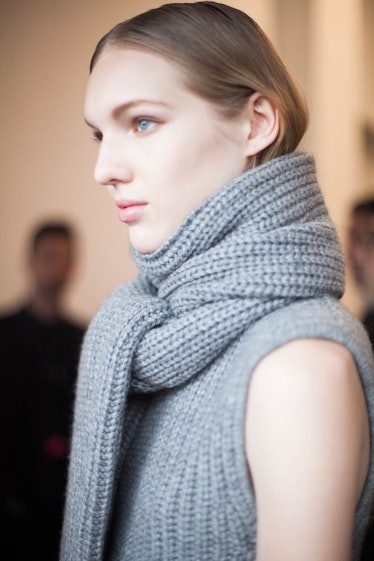 A brunette model posing in a grey woolen scarf and sleeveless sweater
